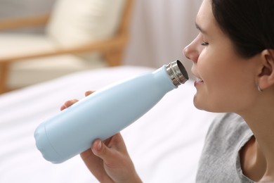 Photo of Woman drinking from thermo bottle in room, closeup