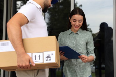 Photo of Woman signing for delivered parcel near entrance outdoors