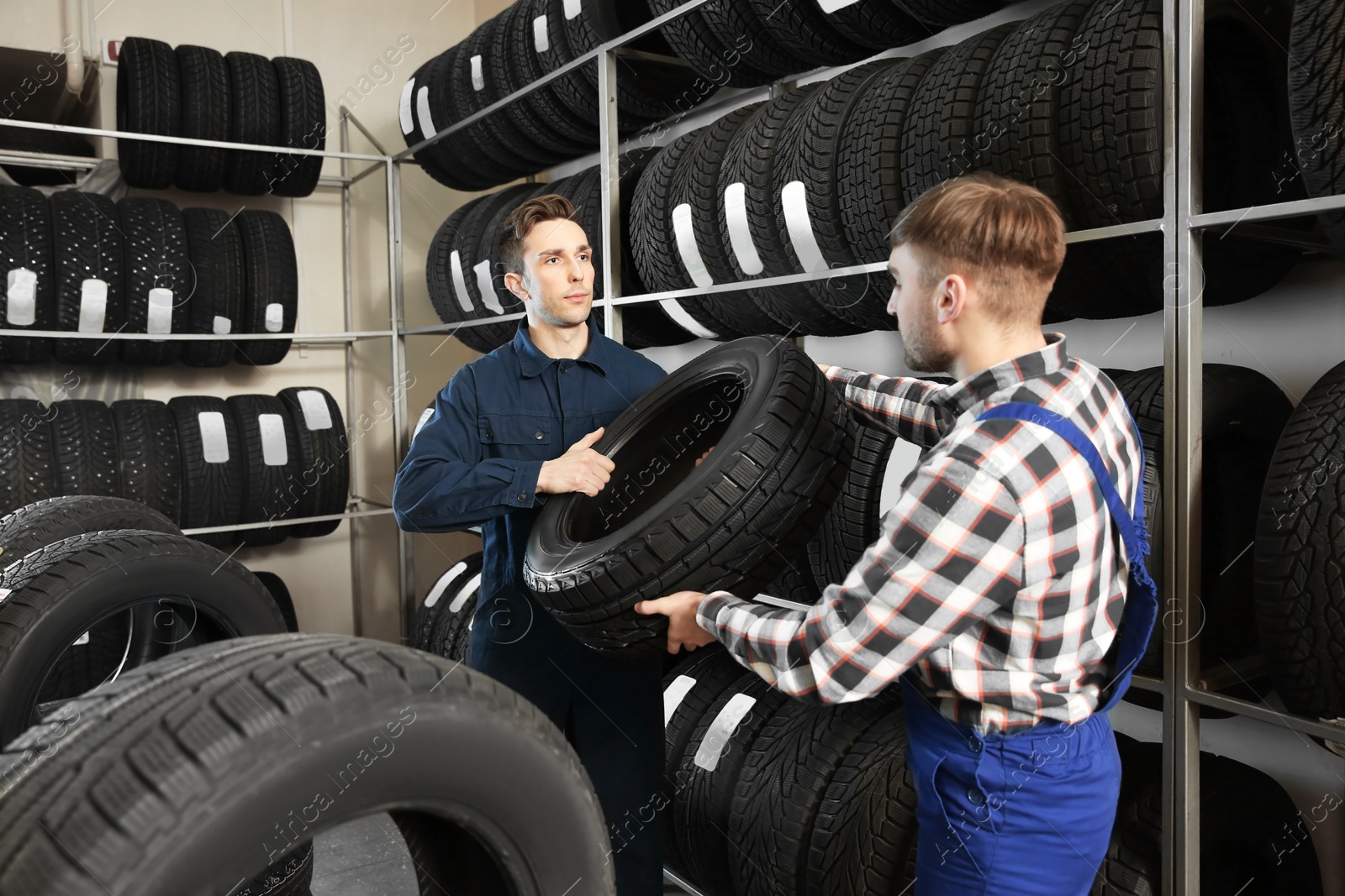 Photo of Young male mechanics with car tires in automobile service center