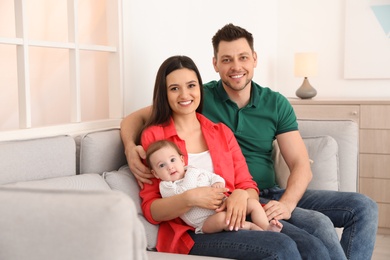 Photo of Happy couple with adorable baby on sofa at home. Family time