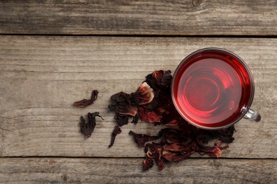 Cup of fresh hibiscus tea and dry flower leaves on wooden table, flat lay. Space for text