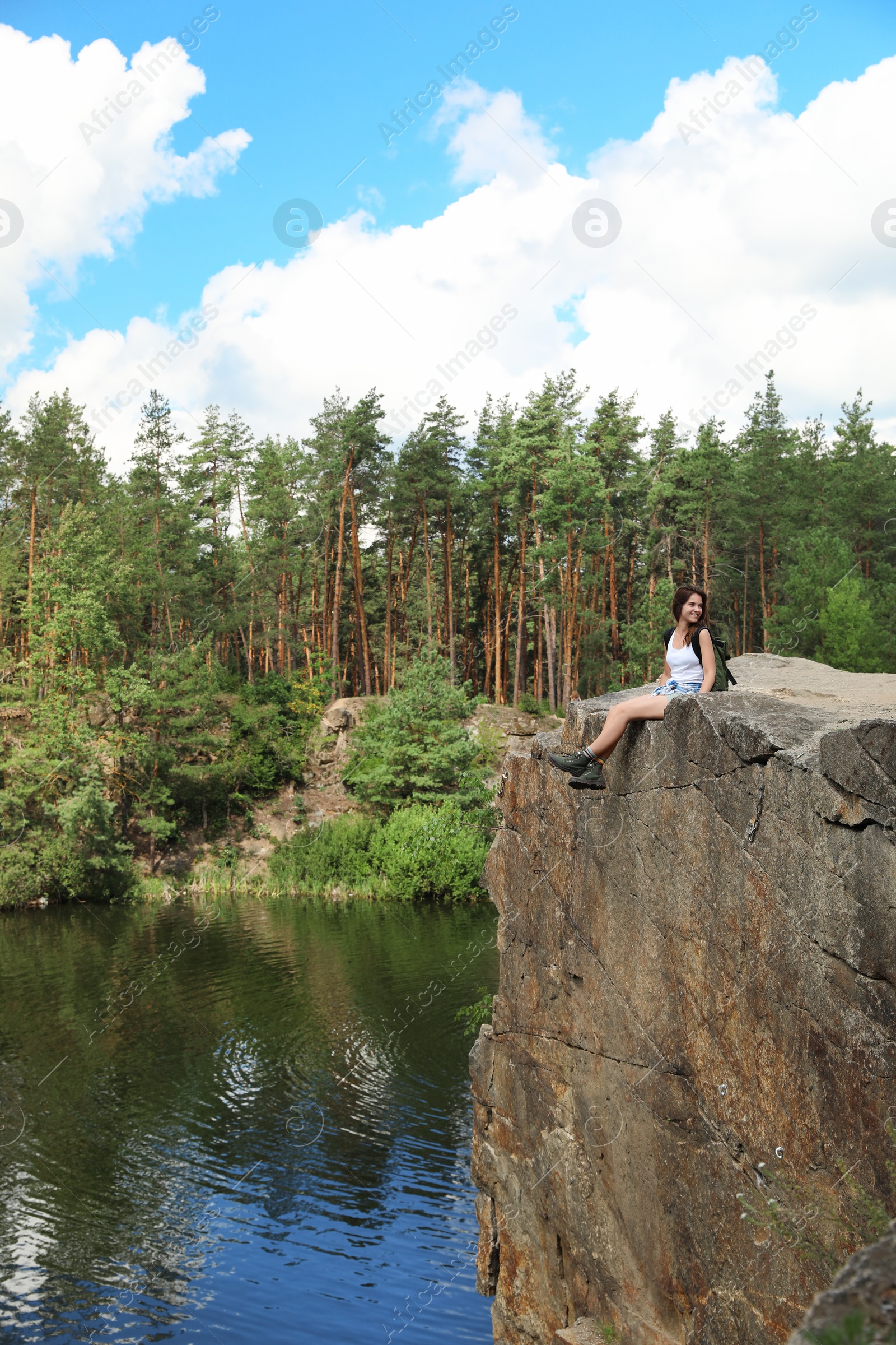 Photo of Young woman on rock near lake and forest. Camping season