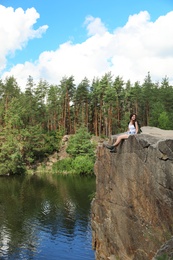 Young woman on rock near lake and forest. Camping season