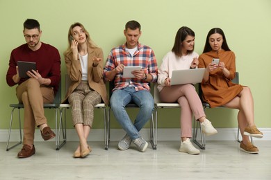 Photo of People waiting for job interview near light green wall indoors