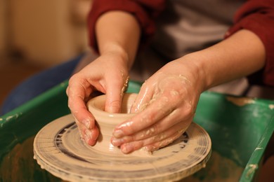 Photo of Woman crafting with clay on potter's wheel indoors, closeup