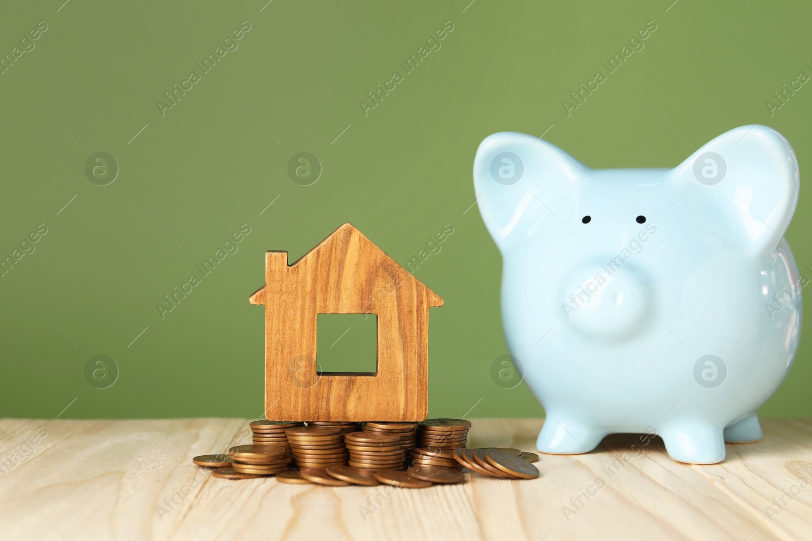 Photo of House model, coins and piggy bank on wooden table against green background, space for text