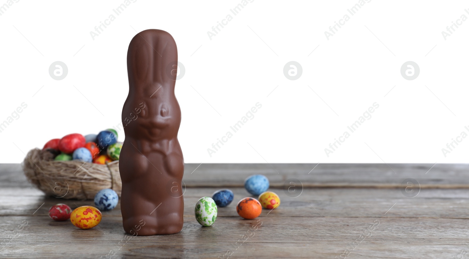 Photo of Chocolate Easter bunny and dyed quail eggs on wooden table against white background. Space for text