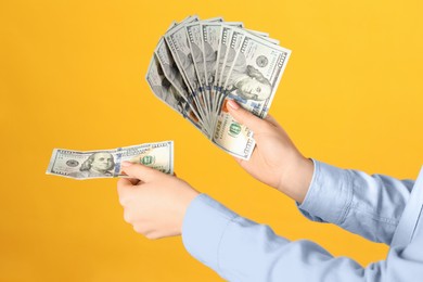Photo of Woman holding dollar banknotes on yellow background, closeup. Money exchange concept