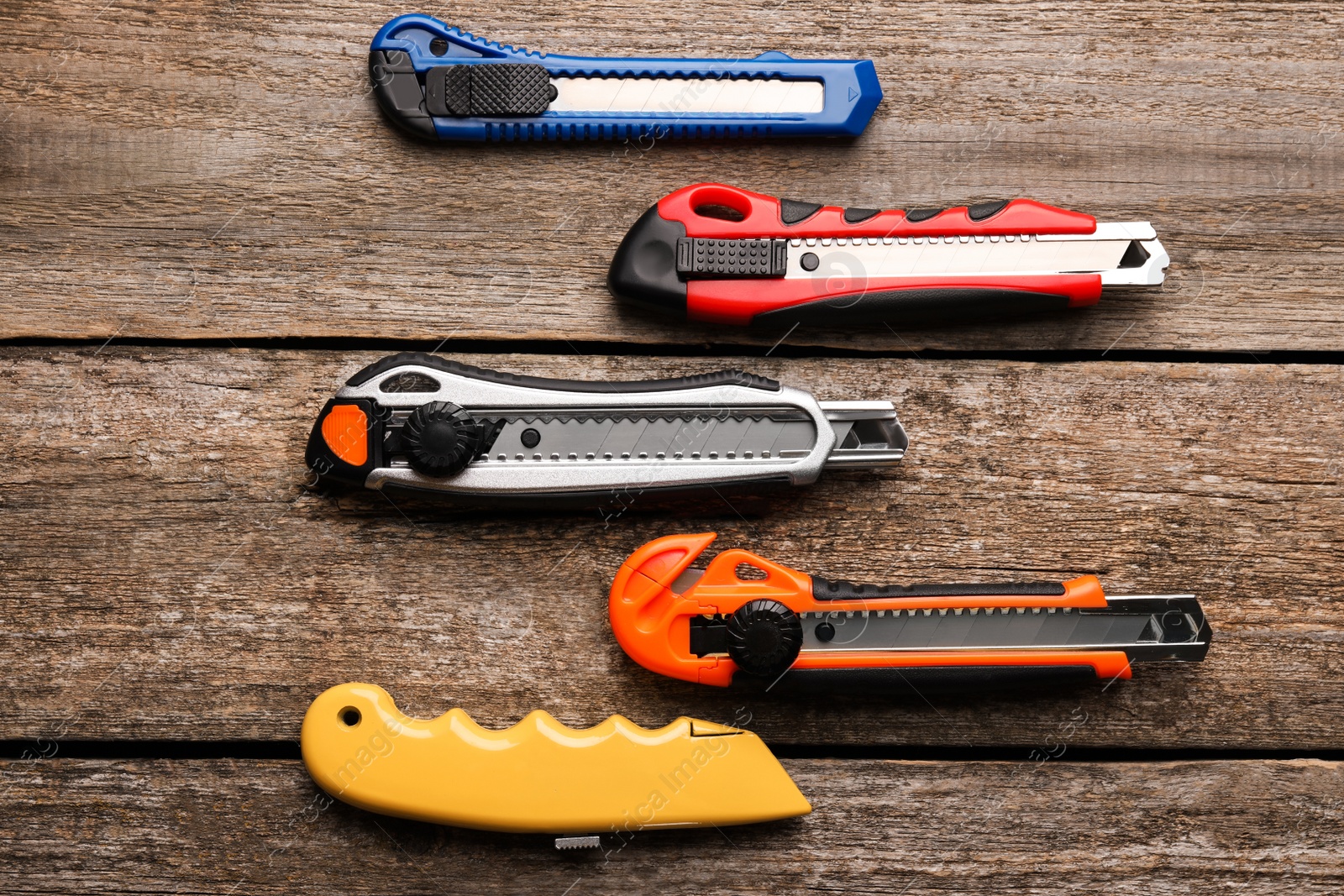 Photo of Different utility knives on wooden table, flat lay