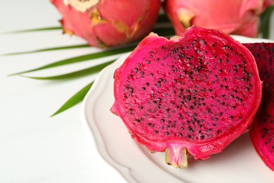 Photo of Plate of delicious cut red pitahaya fruit on white table, closeup