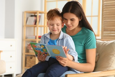 Photo of Mother reading book with her son on armchair in living room at home