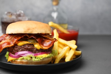 Photo of Tasty burger with bacon, vegetables and patty served with french fries on grey wooden table, closeup. Space for text