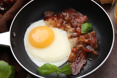 Photo of Fried egg, bacon and basil in frying pan on brown table