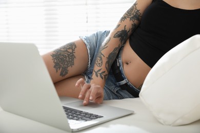 Photo of Beautiful woman with tattoos on body using laptop in living room, closeup
