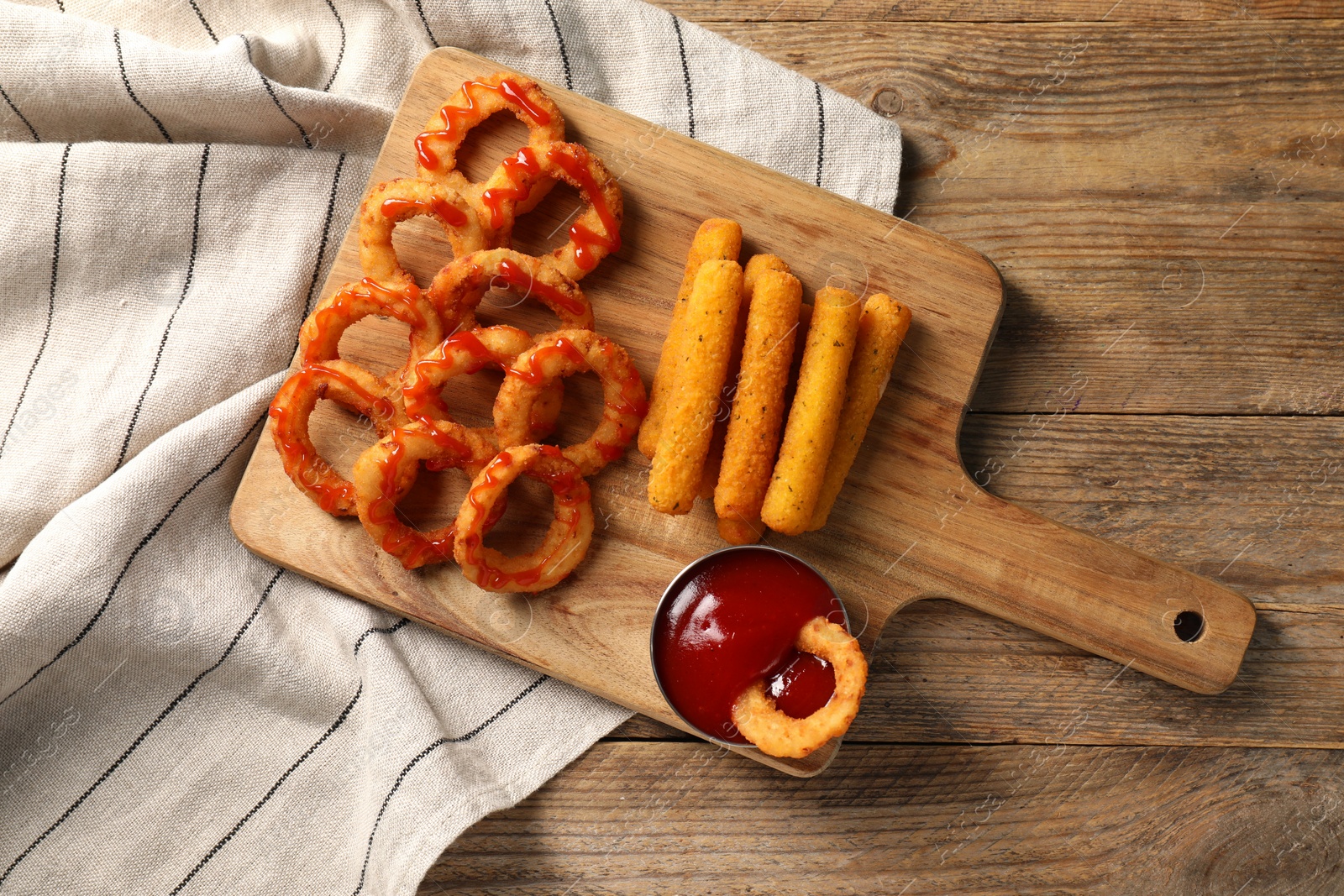 Photo of Tasty fried onion rings, cheese sticks and ketchup on wooden table, top view