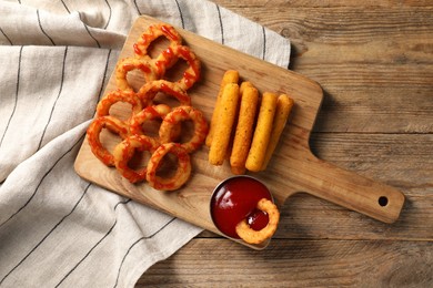 Tasty fried onion rings, cheese sticks and ketchup on wooden table, top view