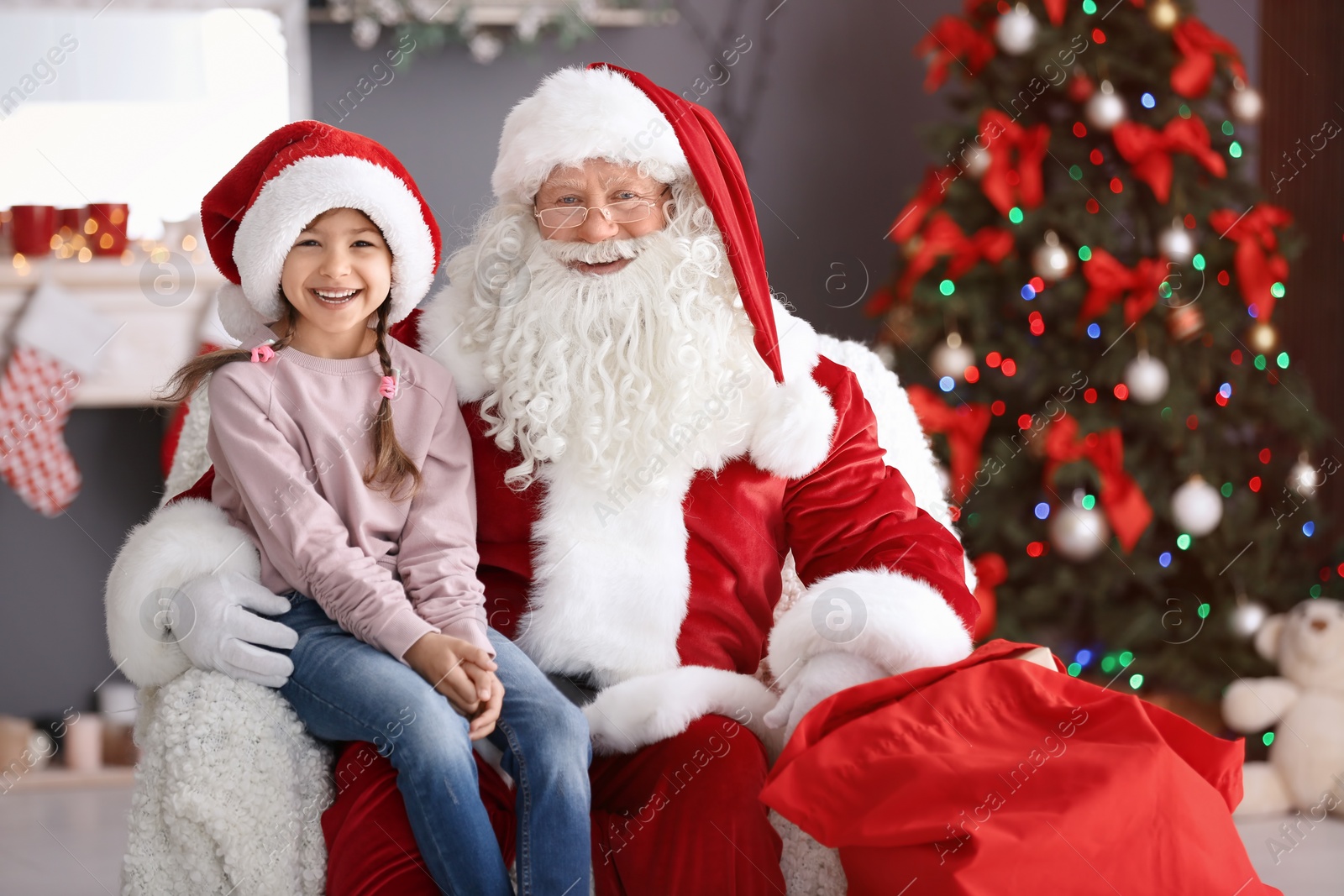 Photo of Little girl sitting on authentic Santa Claus' lap indoors