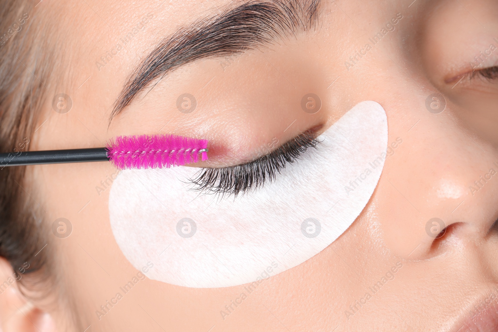 Photo of Young woman undergoing eyelashes extensions procedure, closeup