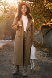 Beautiful African-American woman with stylish white backpack and hot drink on city street