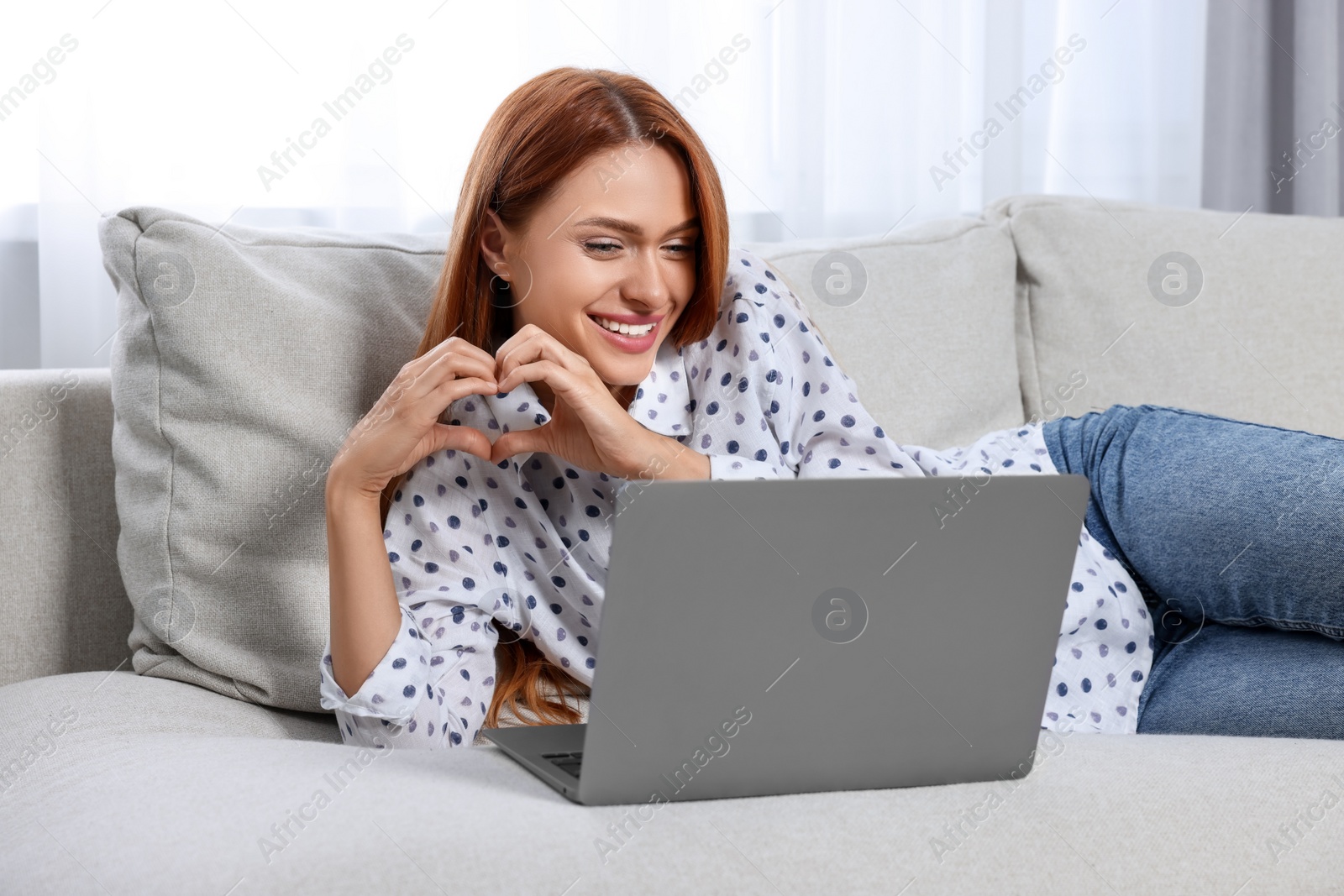 Photo of Woman making heart with hands during video chat via laptop at home. Long-distance relationship