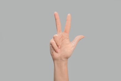 Photo of Woman showing number three on grey background, closeup. Sign language