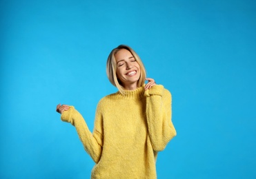 Beautiful young woman wearing knitted sweater on light blue background