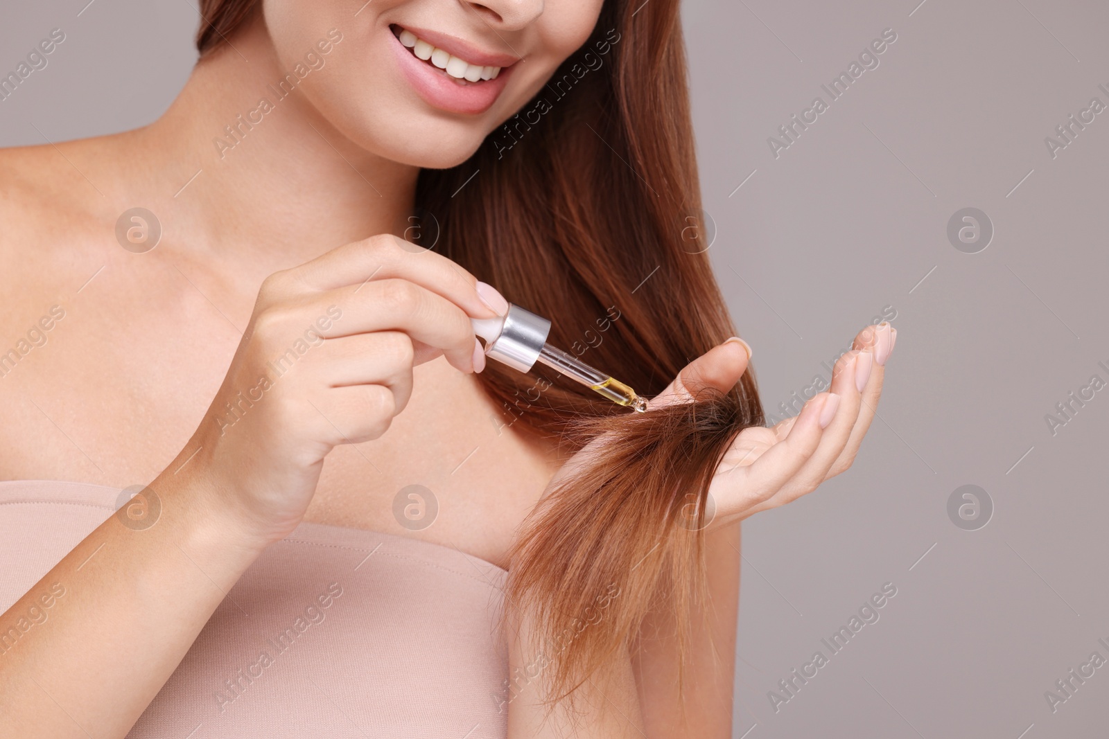 Photo of Woman applying serum onto hair on grey background, closeup