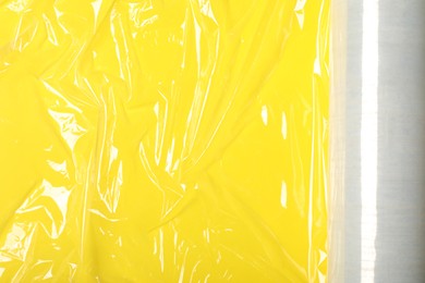 Roll of plastic stretch wrap film on yellow background, top view