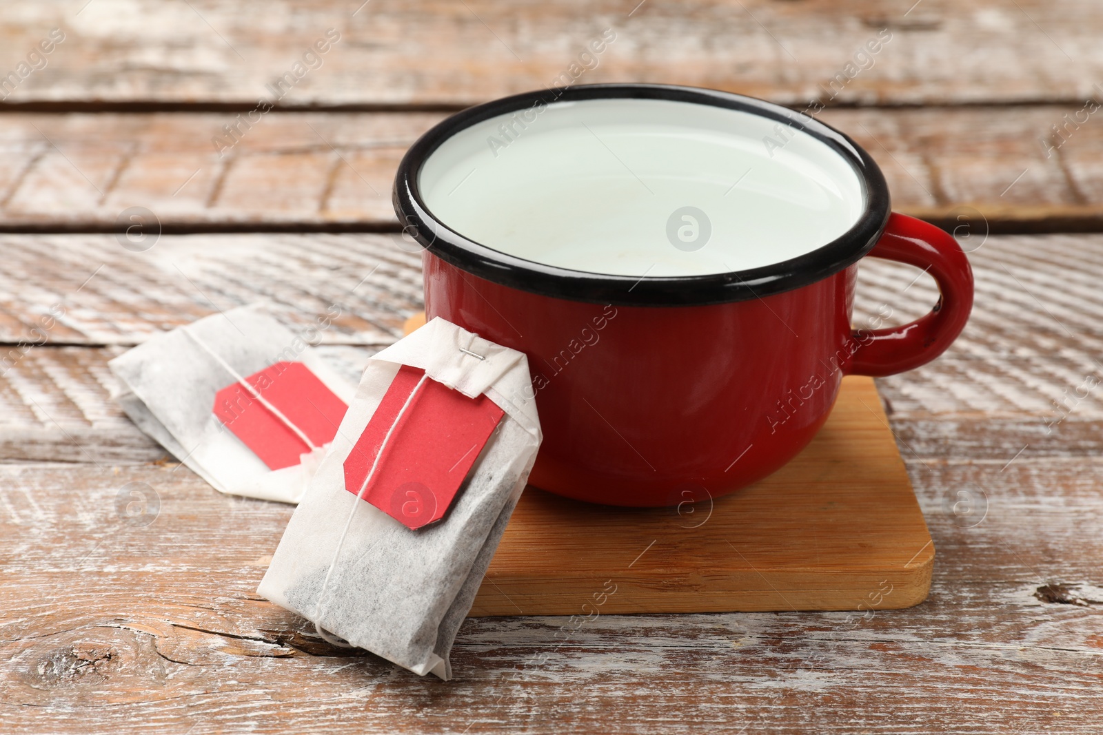 Photo of Tea bags and cup of hot water on wooden rustic table, closeup