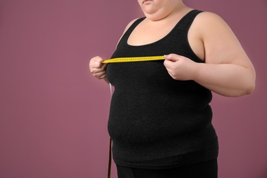 Overweight woman with measuring tape on color background