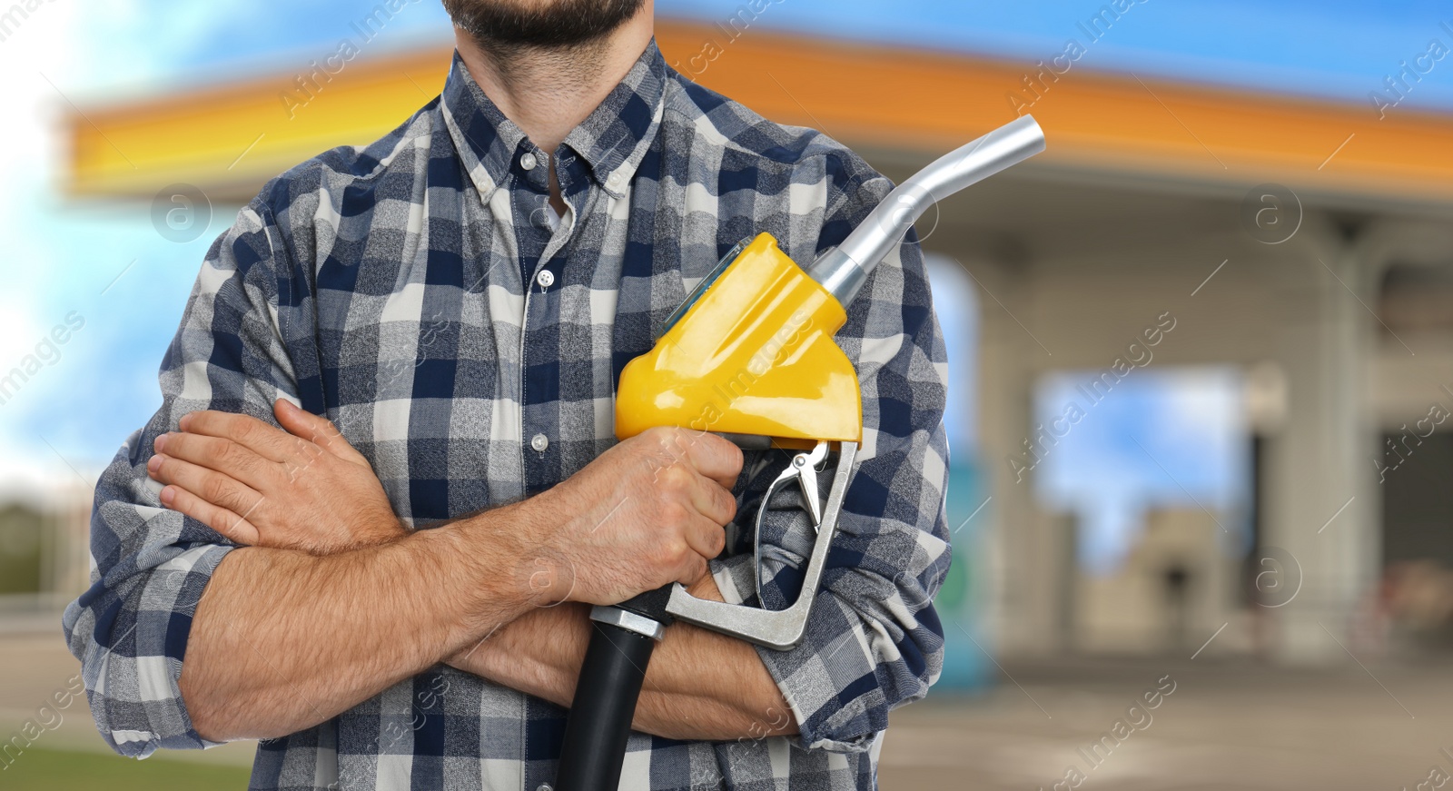 Image of Man holding fuel nozzle near gas station, closeup