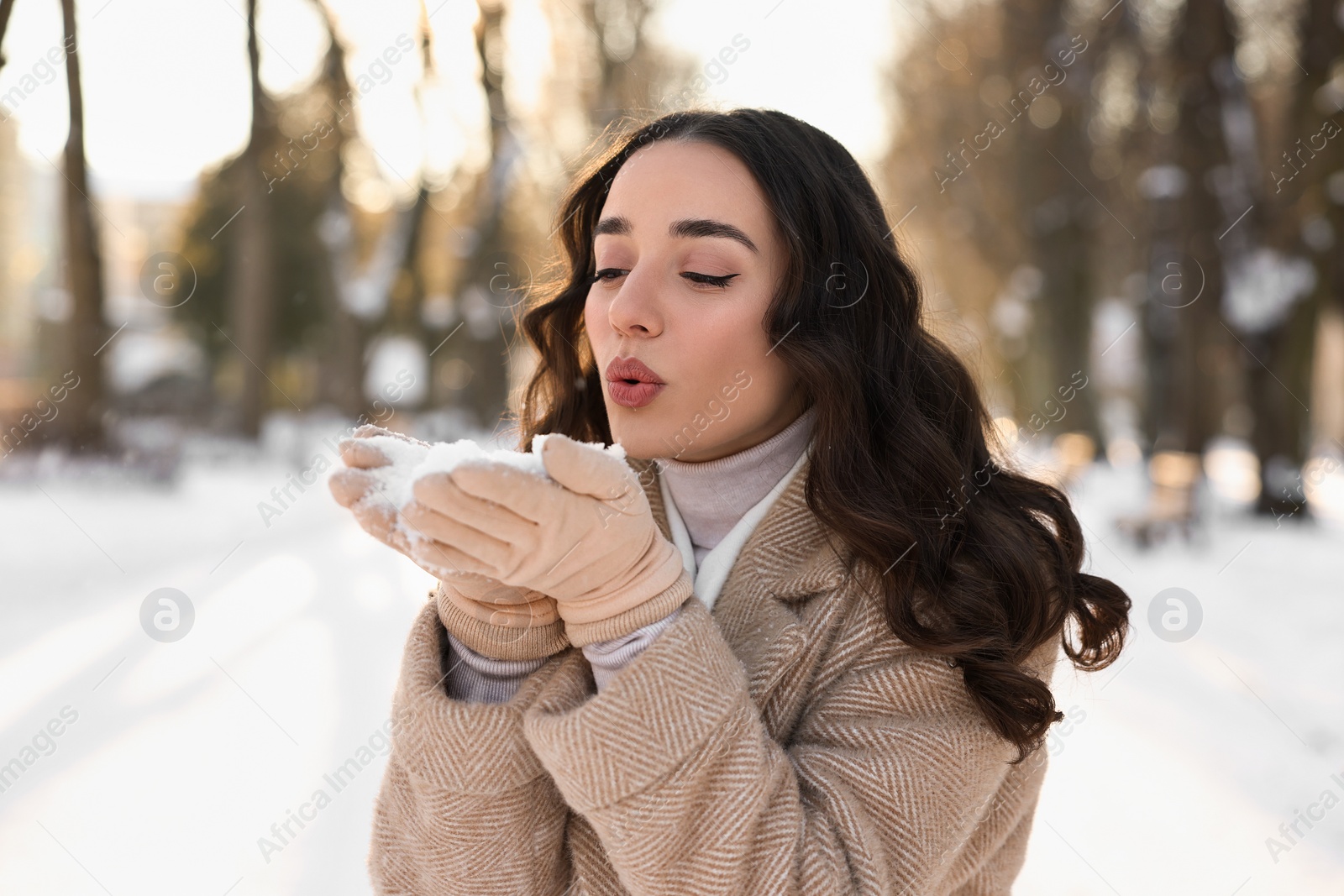 Photo of Portrait of beautiful woman blowing snow from hands in park