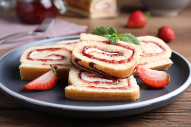 Tasty cake roll with strawberry jam and cream on wooden table, closeup