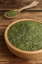 Bowl and spoon of dried dill on wooden table, closeup