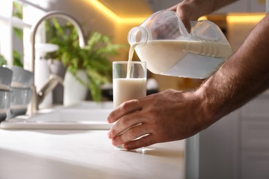 Photo of Man pouring milk from gallon bottle into glass at white countertop in kitchen, closeup
