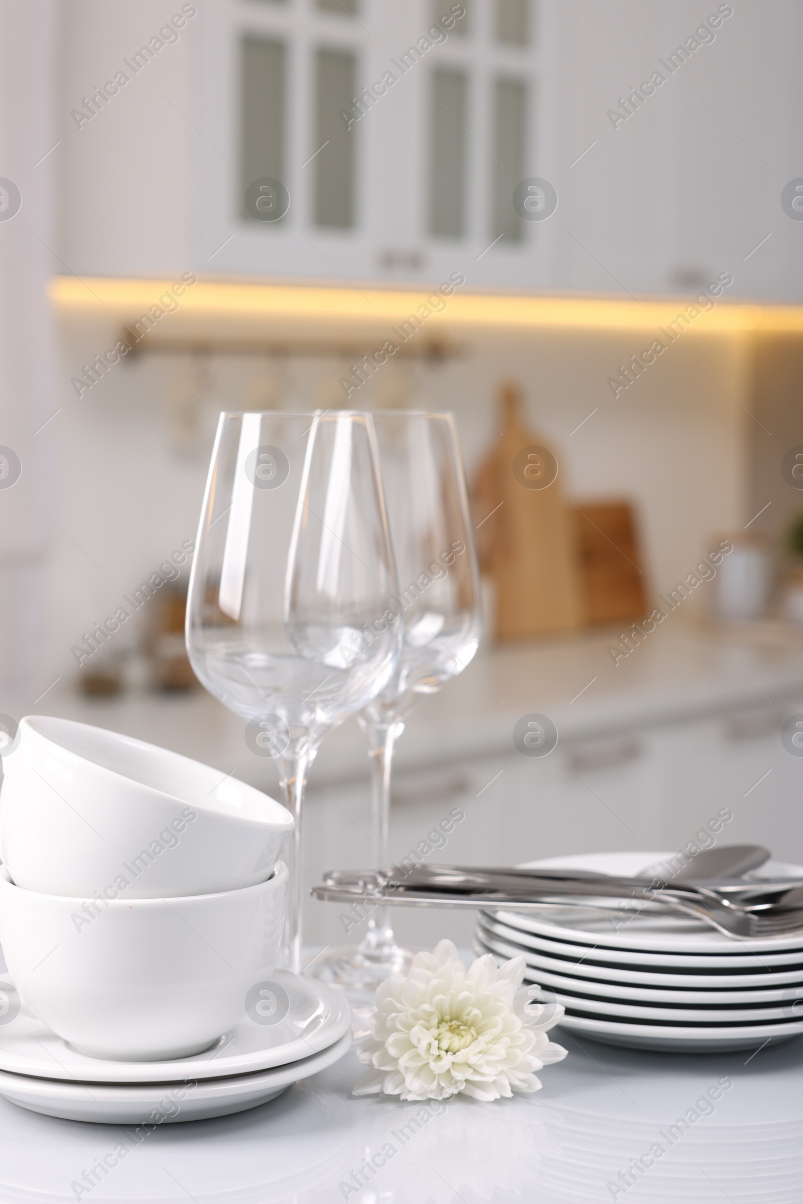 Photo of Set of clean dishware, glasses, cutlery and flower on table in kitchen