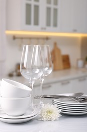 Photo of Set of clean dishware, glasses, cutlery and flower on table in kitchen