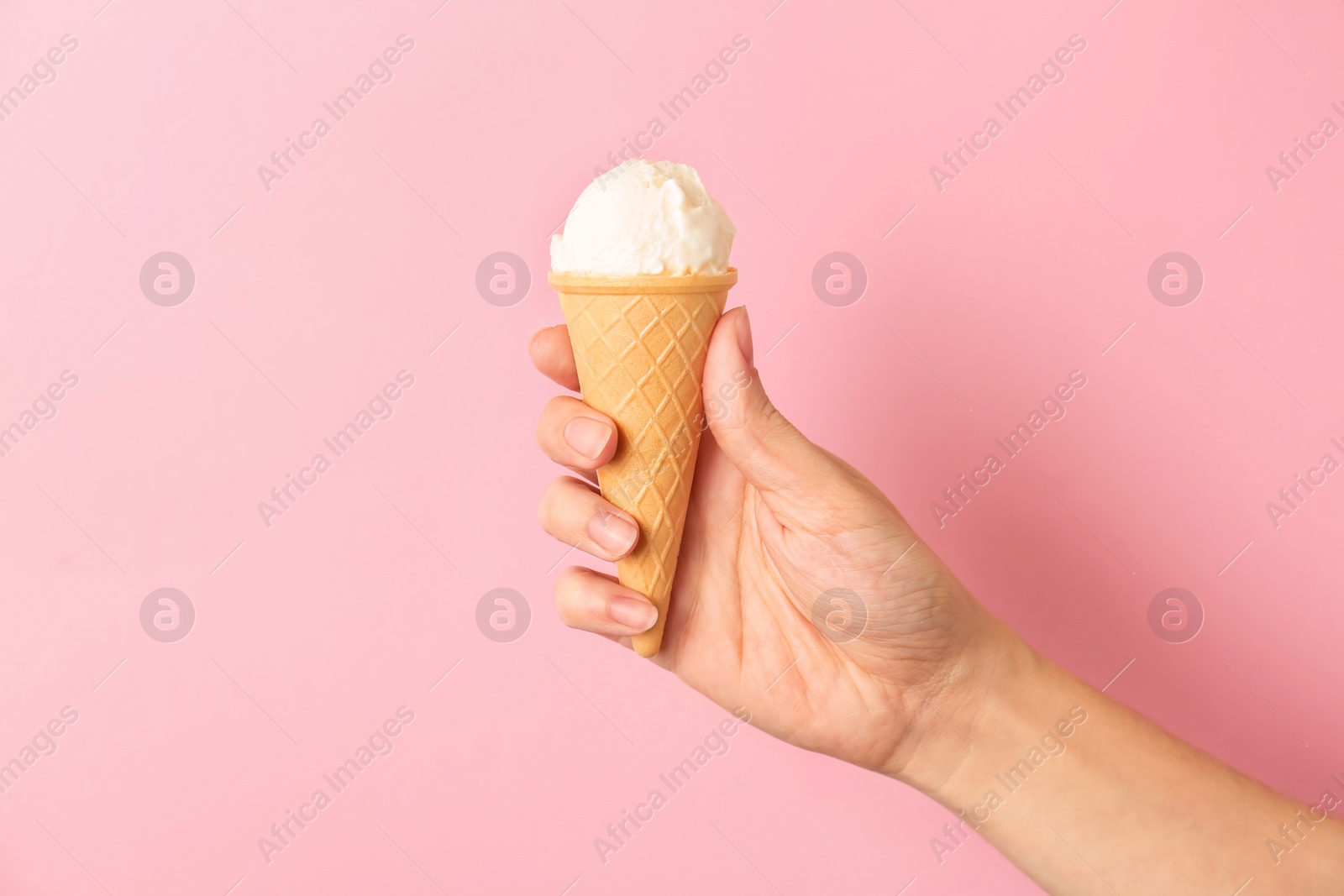 Photo of Woman holding waffle cone with tasty vanilla ice cream on color background