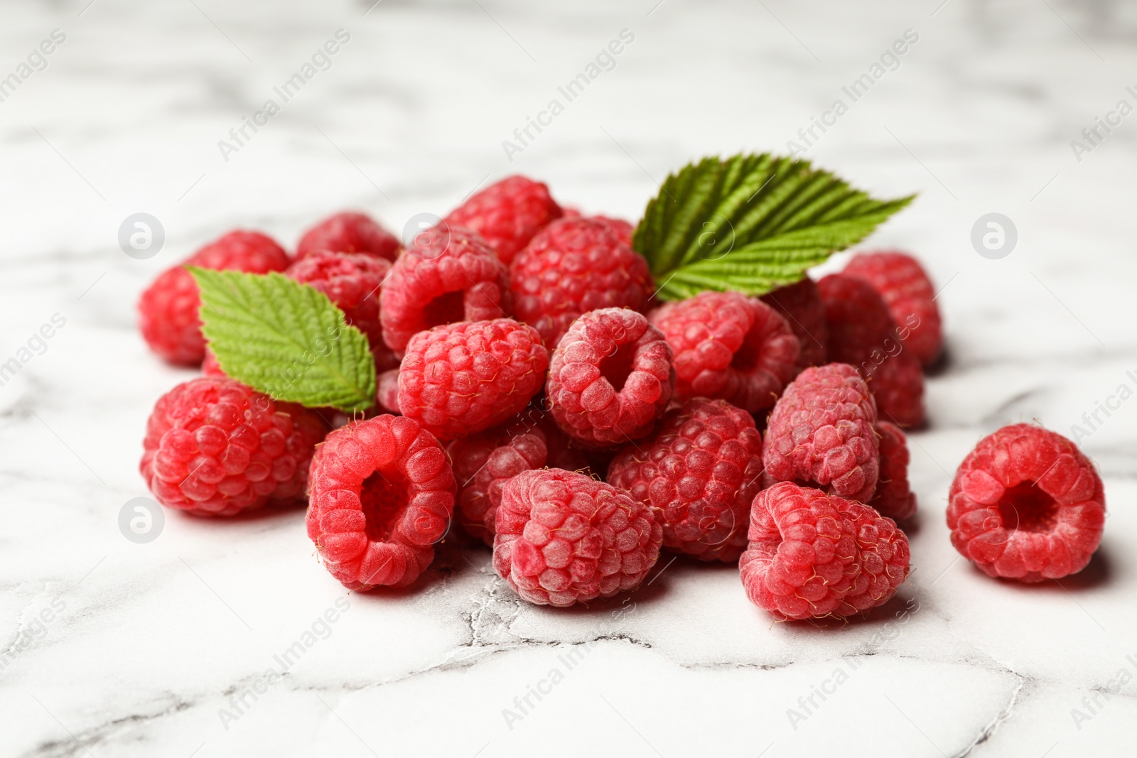 Photo of Heap of delicious ripe raspberries on white marble table, closeup