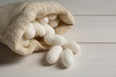 Photo of Silk cocoons with sackcloth bag on white wooden table, closeup