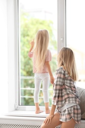 Young woman with cute little girl near window at home