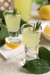 Photo of Tasty limoncello liqueur and green leaves on light textured table, closeup