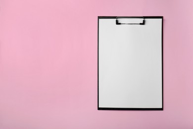 Black clipboard with sheet of blank paper on pink background, top view. Space for text