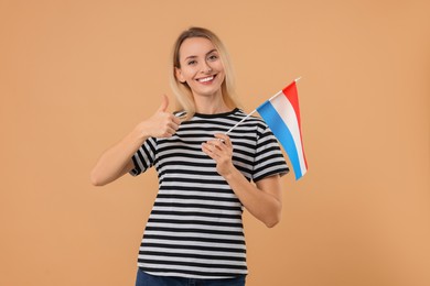 Happy woman with flag of Netherlands showing thumbs up on beige background