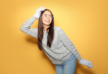 Image of Happy young woman wearing warm sweater and mittens on yellow background