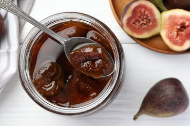 Photo of Jar of tasty sweet jam and fresh figs on white wooden table, flat lay