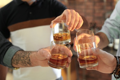 Photo of Friends toasting with glasses of whiskey indoors, closeup