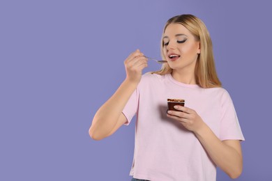 Photo of Woman eating tasty yogurt on violet background. Space for text