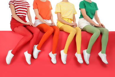 Women wearing bright tights sitting together on color background, closeup