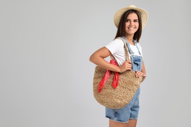 Young woman with stylish straw bag on light grey background. Space for text